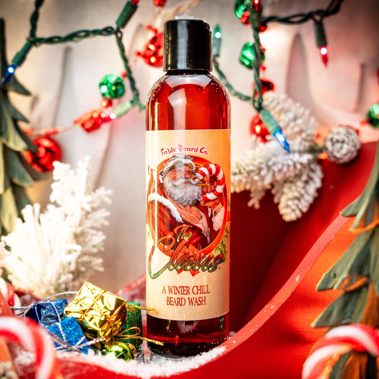 A bottle of 'The Claus' beard wash by Fable Beard Co. placed in a decorative setting with Christmas-themed decorations, including lights and trees, in the background.